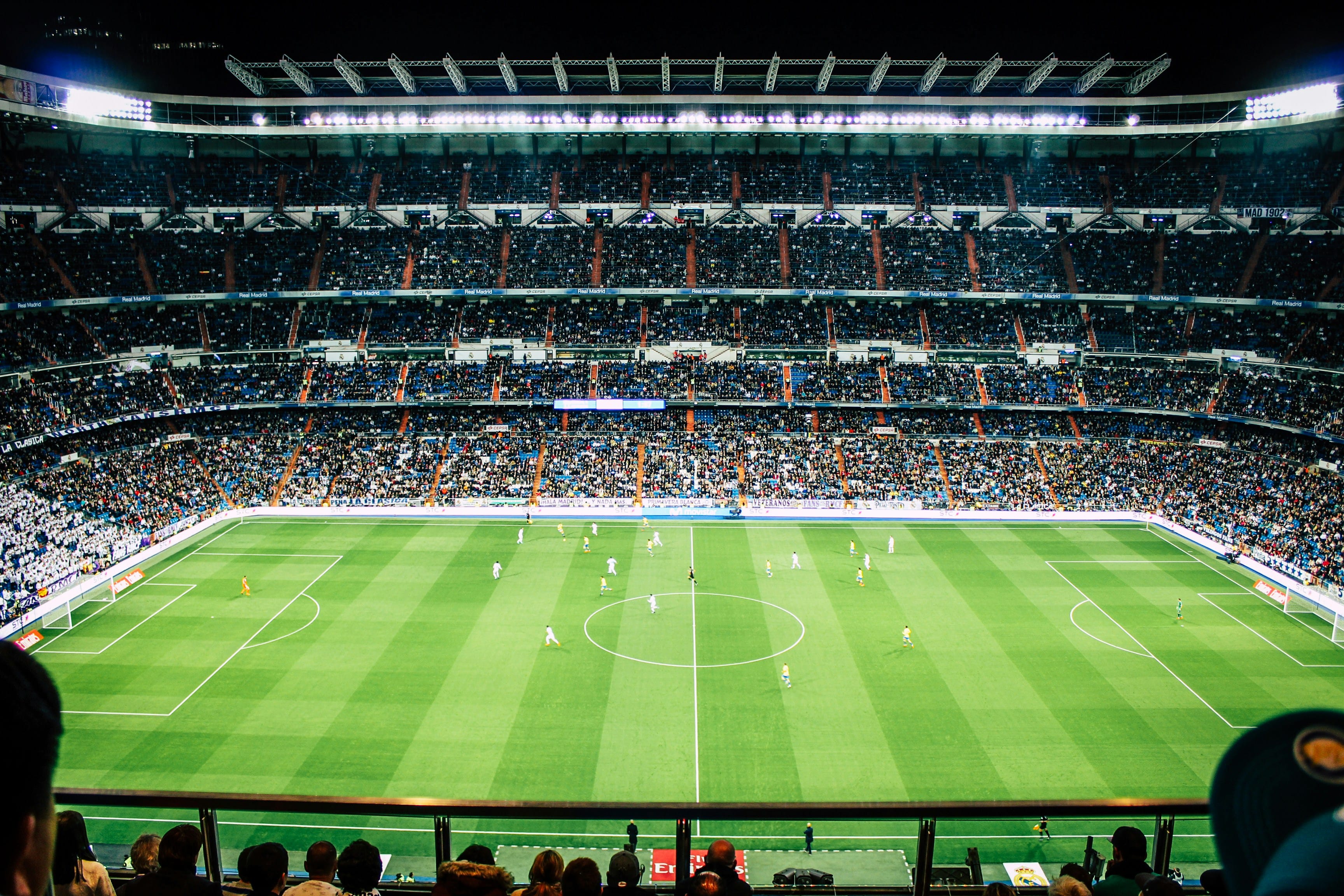 An atmospheric, blurred view of a football stadium at night with bright lights illuminating the pitch.